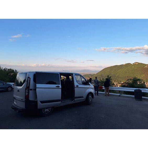A white van parked on a road with a scenic view of hills and a clear sky. 4