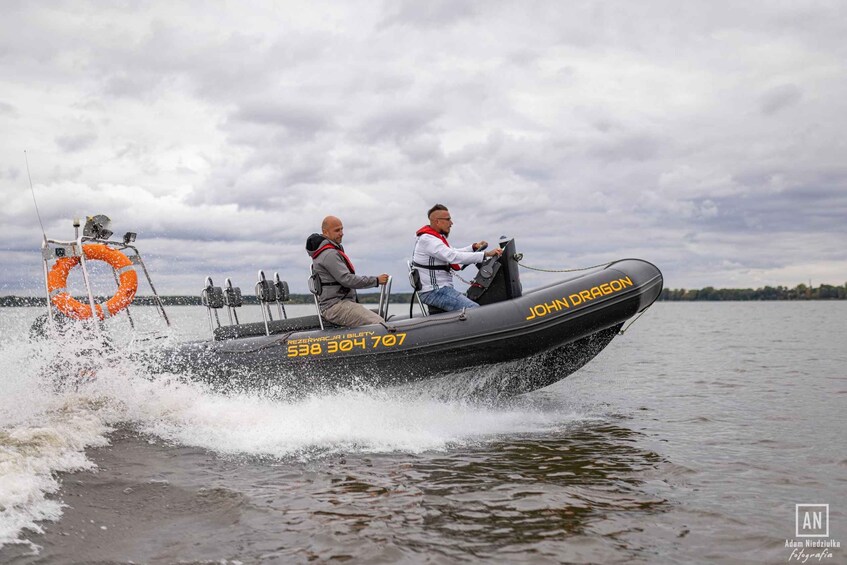 A speedboat with two people, one driving and one as a passenger, on a lake. 2