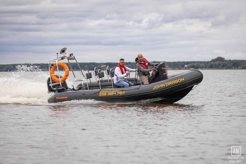 A speedboat with two people wearing life jackets, a radar, and a life preserver on the back. 3