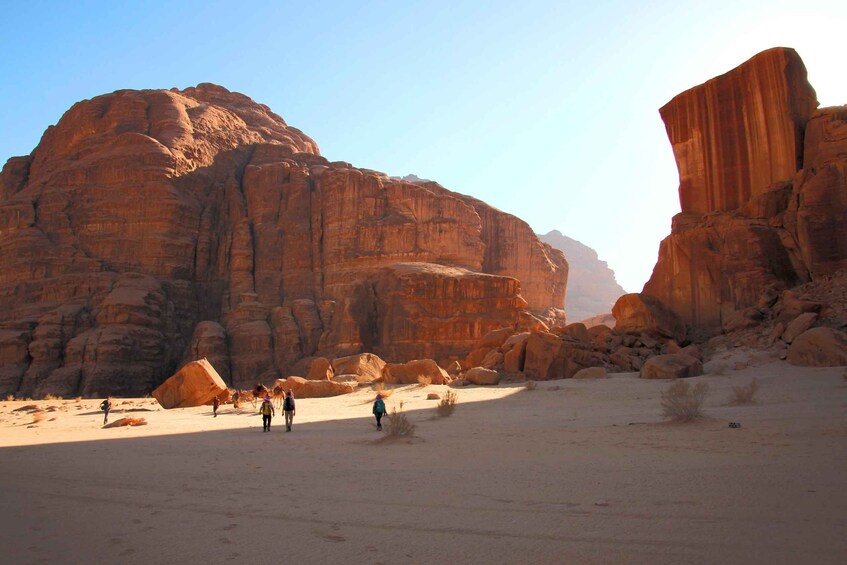 A desert landscape with large sandstone rock formations and a few people walking. 5