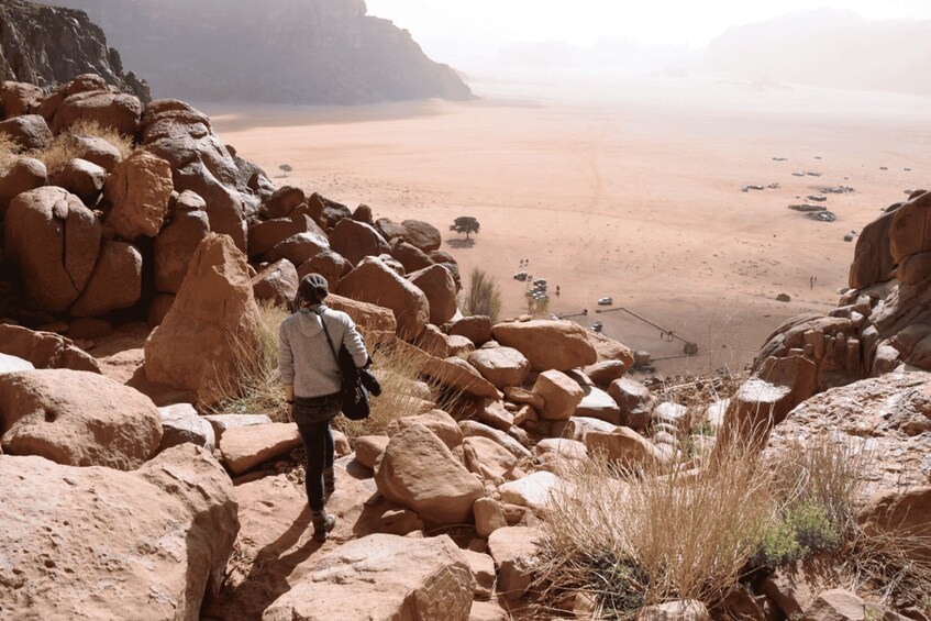 A person hiking through a rocky desert landscape with large boulders and sparse vegetation. 2