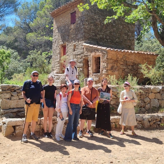 A group of people standing in front of a stone building with a tiled roof, surrounded by trees and a stone wall. 4