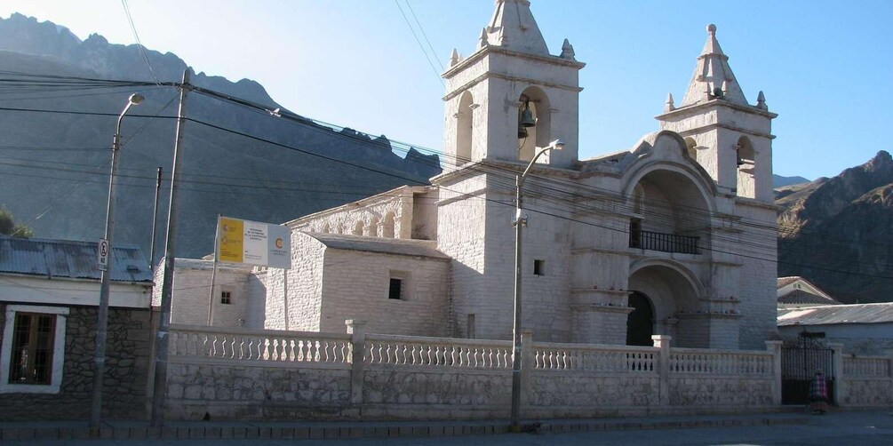 A historic church with two bell towers and a stone facade, surrounded by mountains. 1