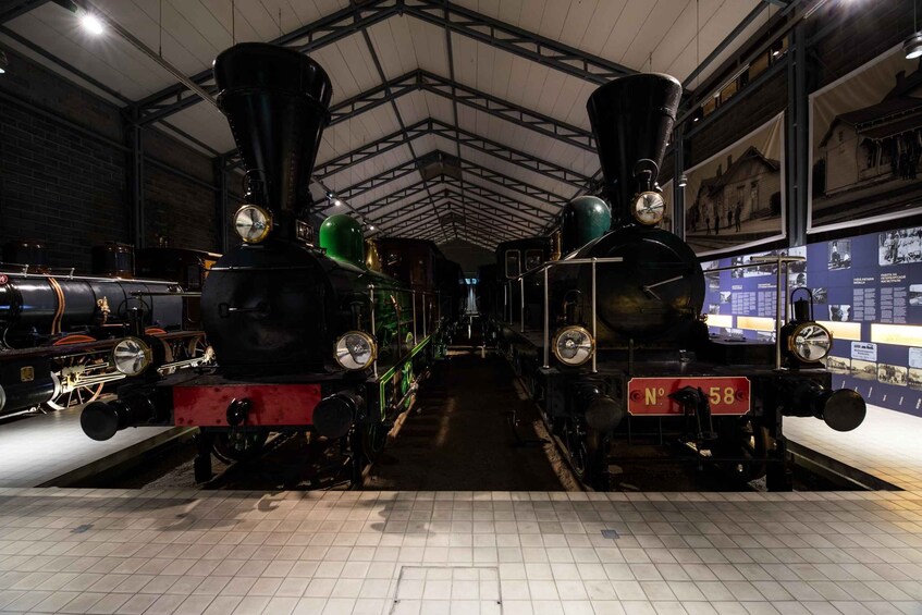 Two vintage steam locomotives at a museum with a tiled floor and brick walls. 2