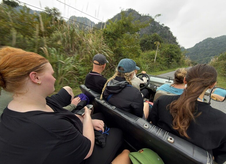 A group of people in a vehicle driving through a forested area with hills in the background. 1