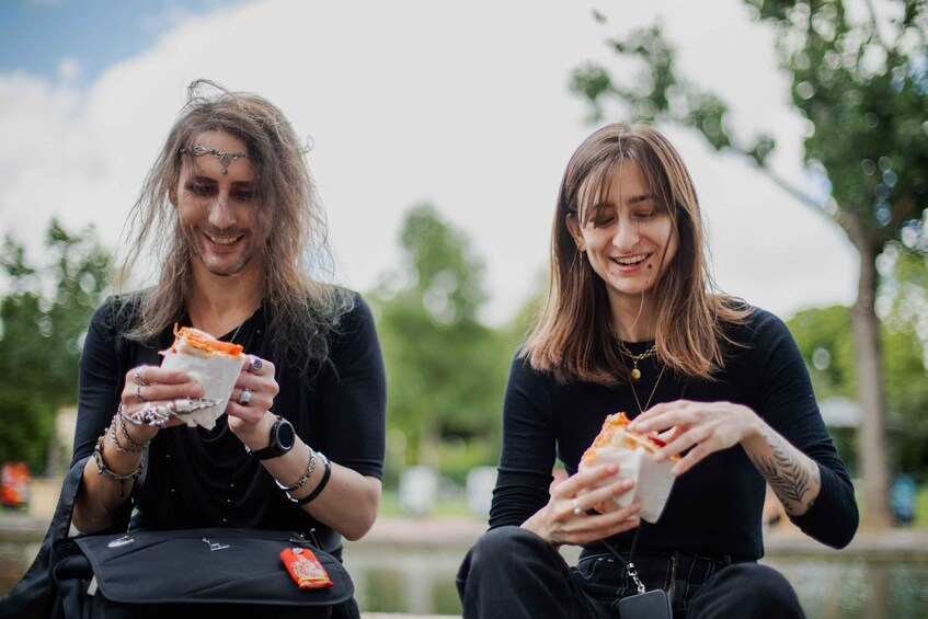 Deux personnes sont assises à l’extérieur et mangent des sandwichs. 2