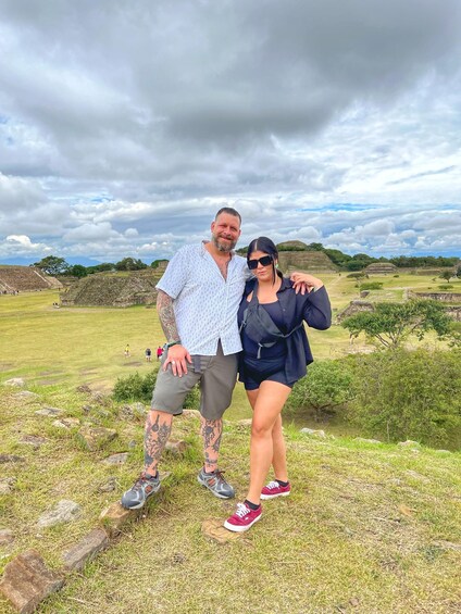 A couple standing in a grassy field with ancient ruins in the background. 1