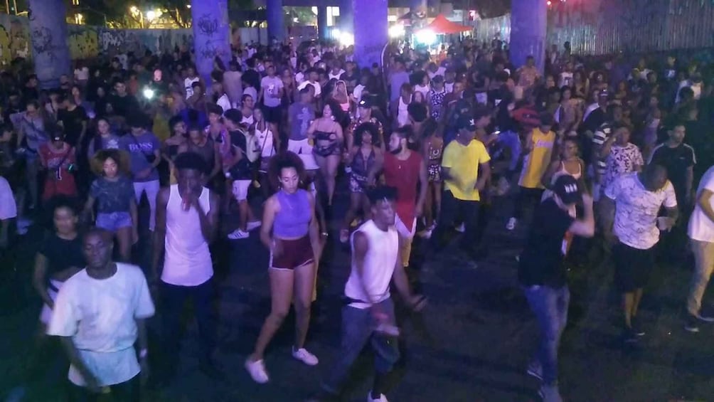 A crowded outdoor event at night with people dancing and socializing. 1