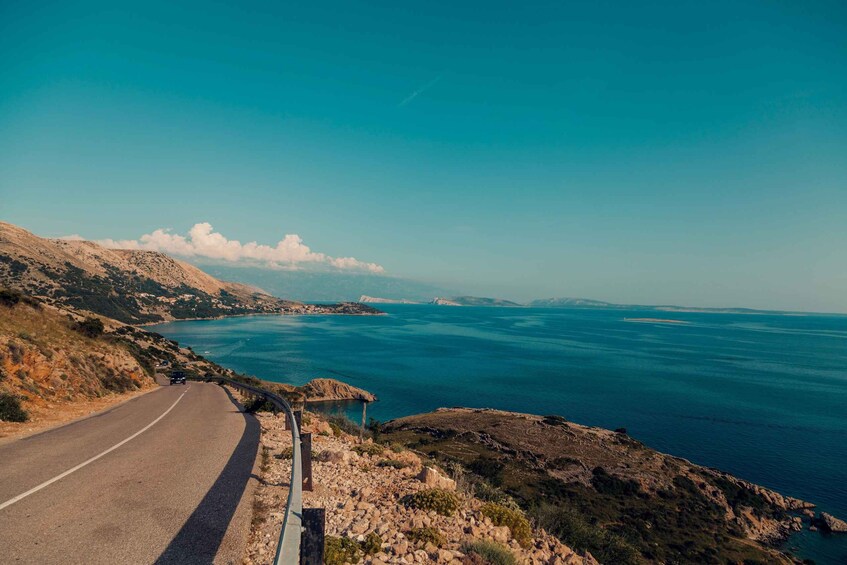 A coastal road curving along a rocky shoreline with a view of the sea and distant landforms. 4