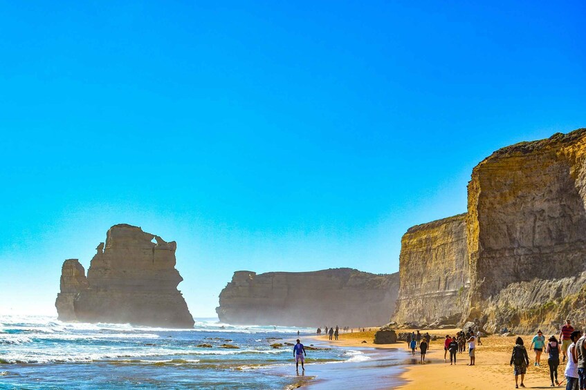 A beach with large rock formations and people walking along the shore. 1
