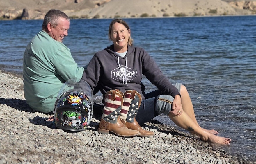 Two people sitting by a rocky shore with a body of water in the background. 1