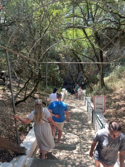 A group of people walking on a stone pathway through a forested area with a metal archway overhead. 2