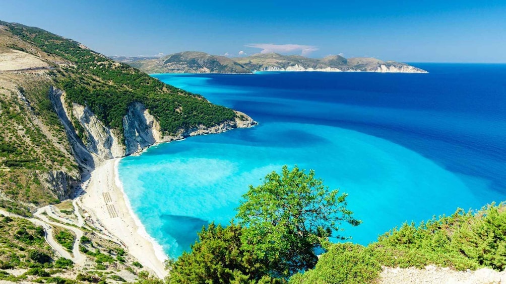 A coastal landscape with a clear blue sea, a sandy beach, and green hills. 1