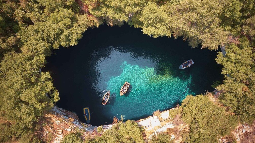 A circular lake surrounded by dense forest, with three boats anchored in the clear water. 3