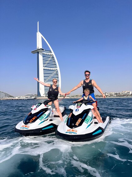 Two people jet skiing on a body of water with a sail-shaped building in the background. 1