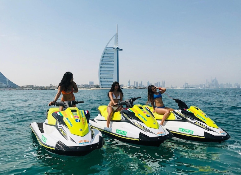 Three women on jet skis in the water with a city skyline in the background. 4