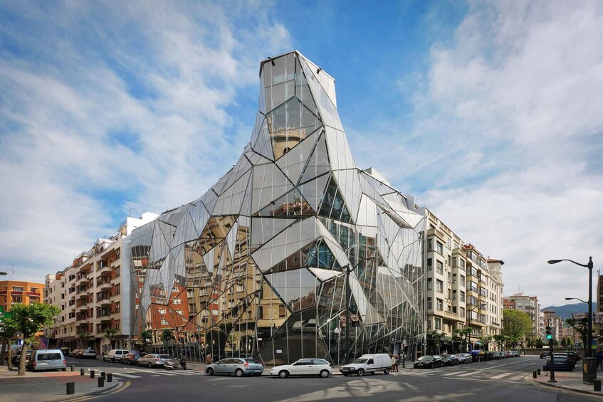 En modern byggnad med en unik, geometrisk design, omgiven av andra byggnader i stadsmiljön och en livlig gata. 5