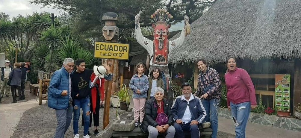 A group of people posing in front of a traditional Ecuadorian structure with a thatched roof. 5