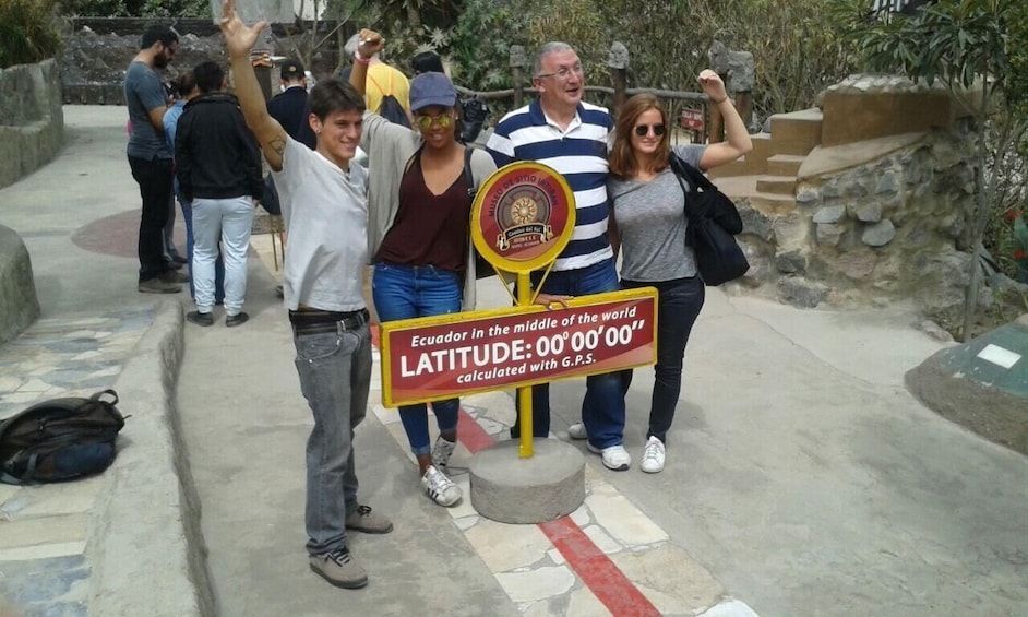 A group of people standing in a stone pathway with a sign stating 'Ecuador in the middle of the world' and 'Latitude:00°00'00''. 4
