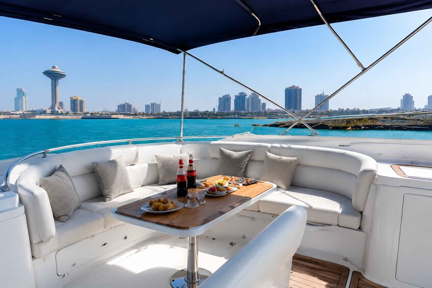A boat with a white leather couch, a wooden table with food and drinks, and a city skyline in the background. 3