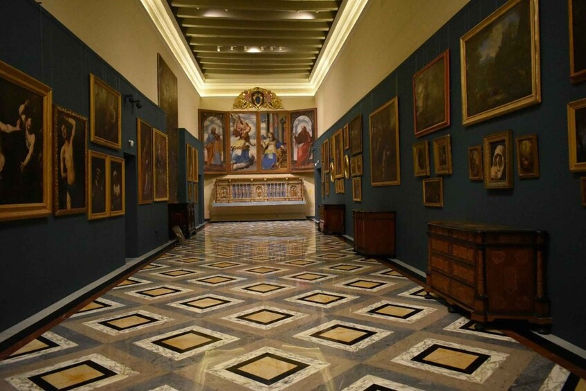 A hallway with a patterned floor, framed paintings on the walls, and a central altar. 3