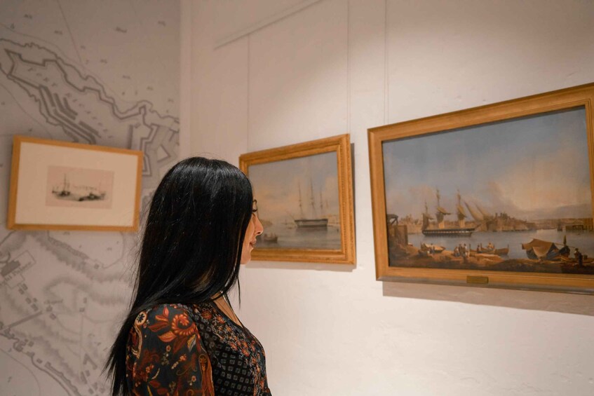 A person viewing paintings of ships on a wall. 1