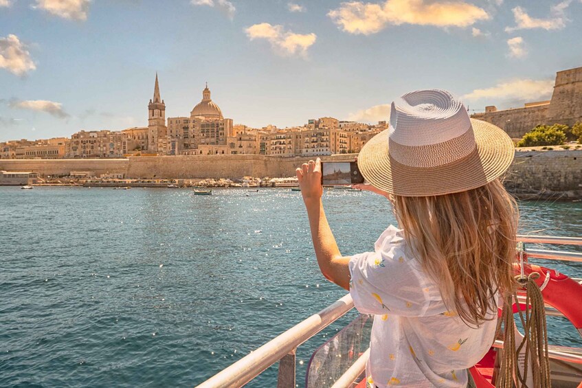 A person on a boat, wearing a straw hat, looking at a city with historic buildings and a prominent tower. 2
