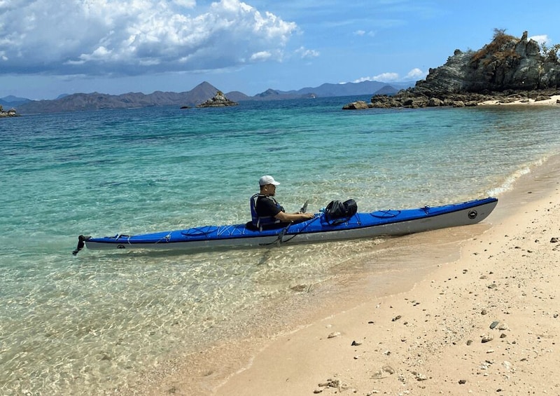 A person in a kayak on a beach with clear water and distant mountains. 4