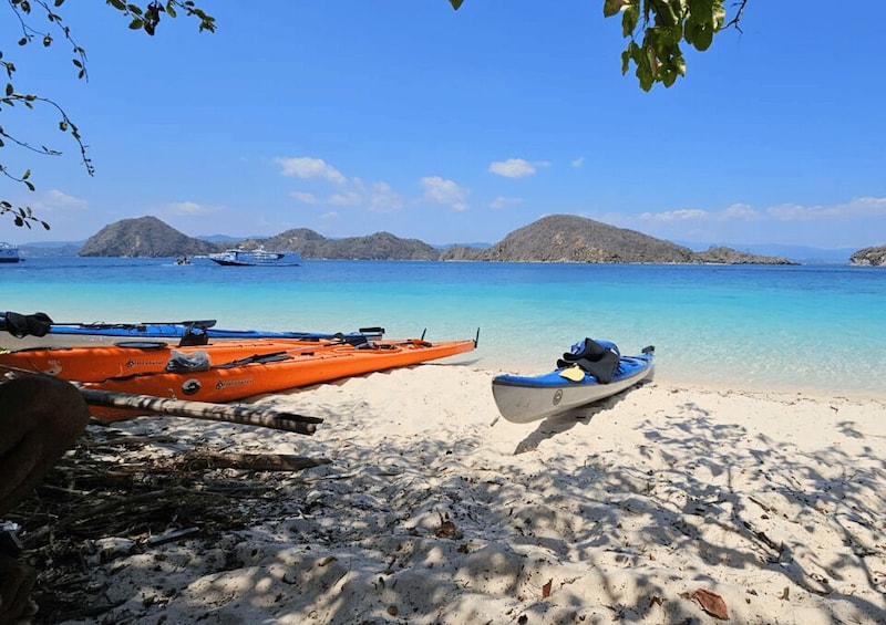 A beach with kayaks and a boat, surrounded by clear water and distant islands. 3