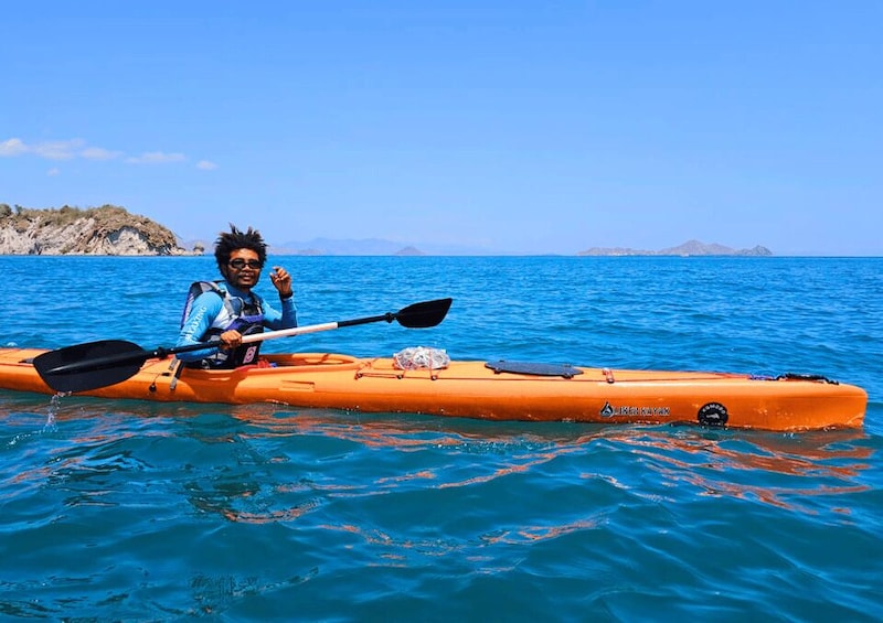 A person kayaking on a clear blue sea with distant rocky islands. 1