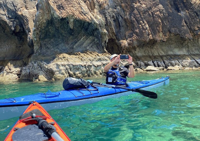 A person kayaking in clear water with rocky cliffs in the background. 2