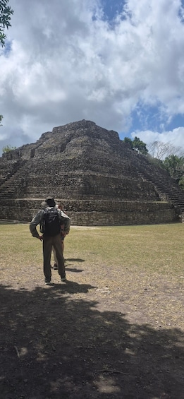 A person standing in a grassy area with a large ancient stone structure in the background. 2