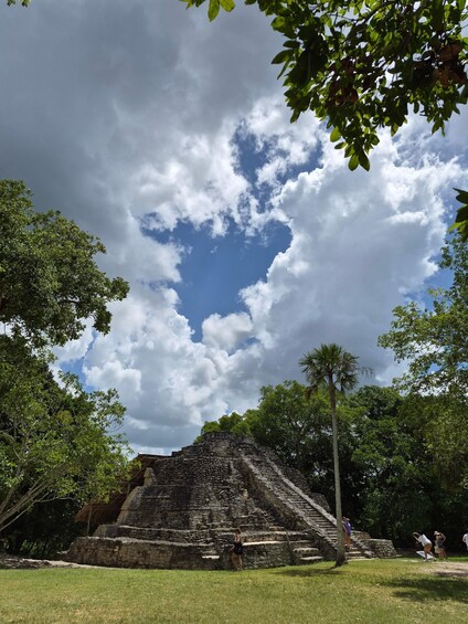 A stone pyramid structure surrounded by lush greenery and a partly cloudy sky. 5