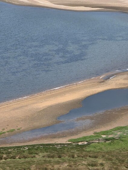 A coastal landscape with a sandy beach, a small inlet, and grassy areas. 3