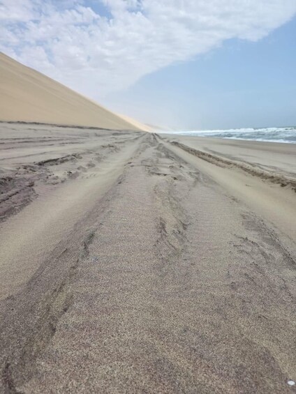 A sandy beach with footprints leading towards the ocean under a partly cloudy sky. 4