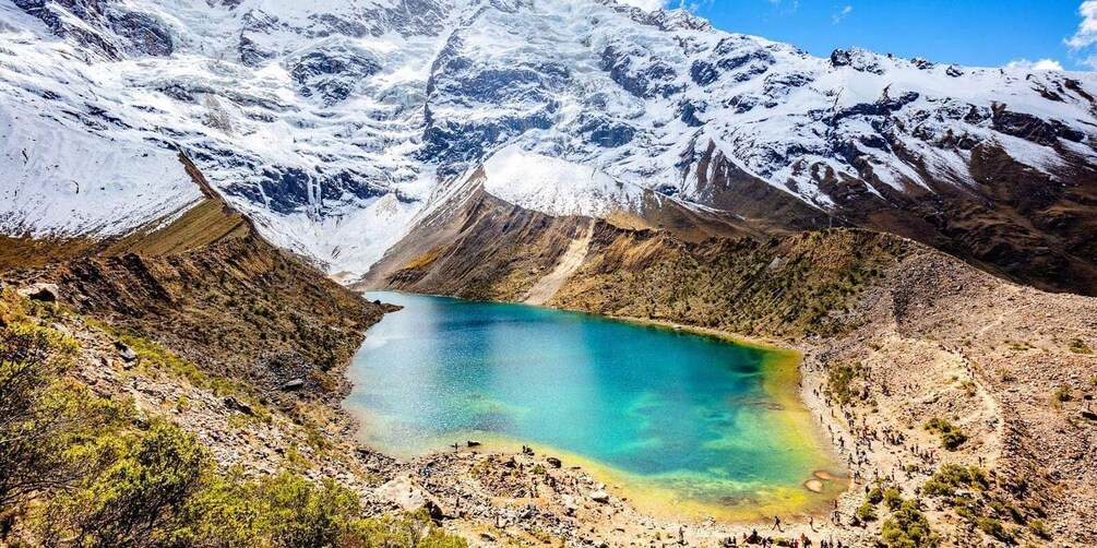 Un lago color turchese circondato da montagne innevate e terreno roccioso. 5