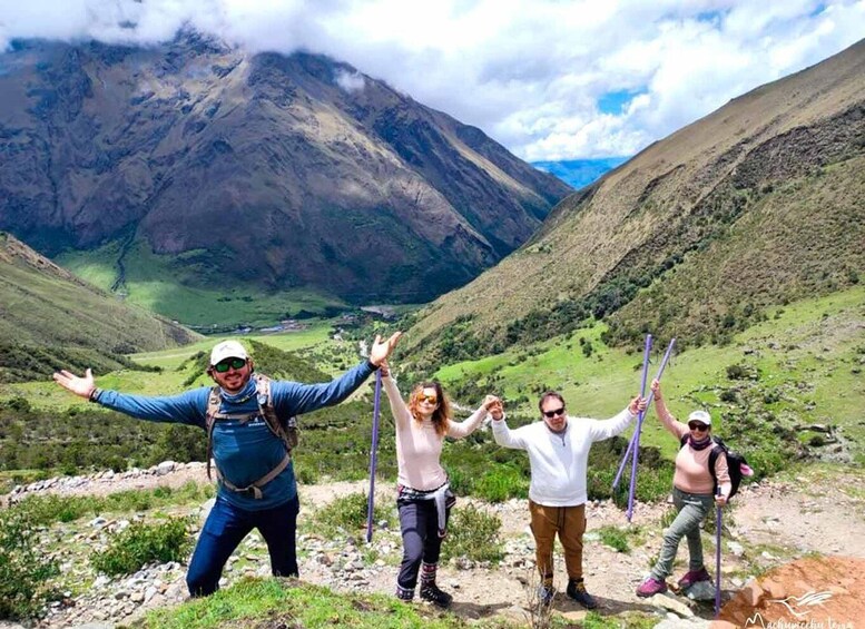 Quattro persone che fanno un'escursione su un sentiero di montagna, con una valle e montagne sullo sfondo. 2
