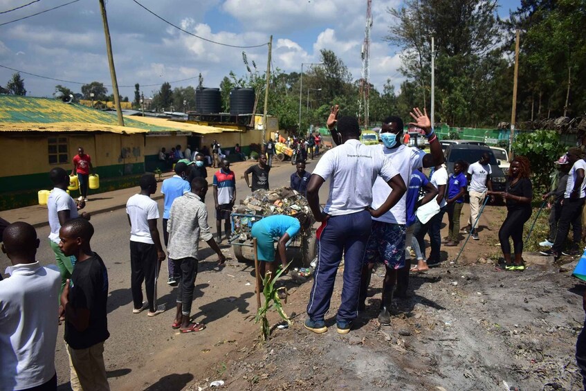 A group of people gathered on a street, some carrying yellow containers, with buildings and trees in the background. 4