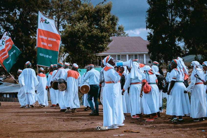 A group of people in traditional attire with flags, standing on a dirt ground. 3