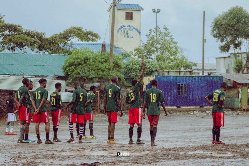 A group of soccer players in green and red uniforms standing on a muddy field. 2