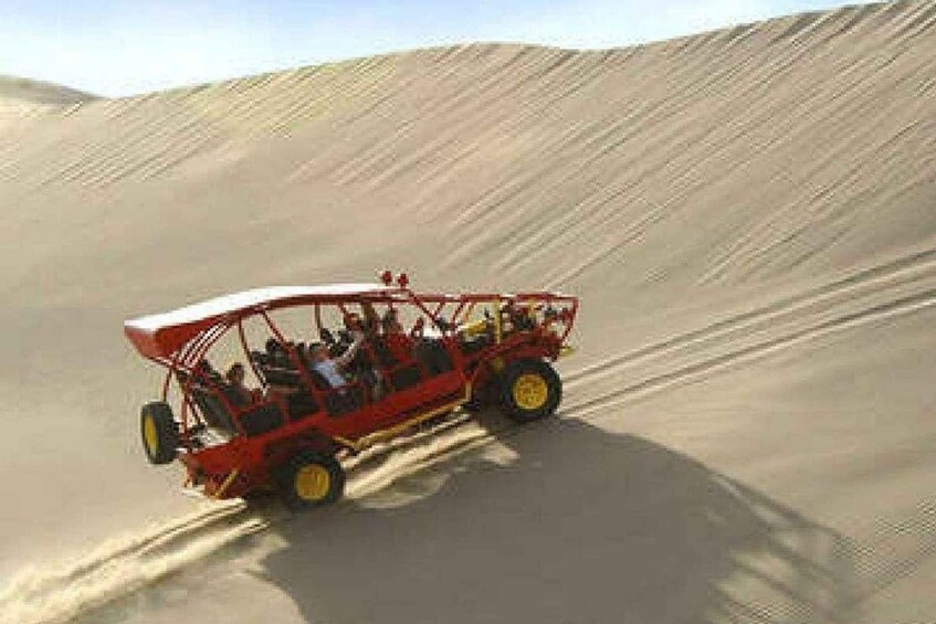 Un vehículo todoterreno rojo circulando por un desierto con dunas de arena. 2