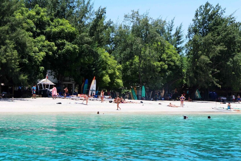 A beach with clear turquoise water, people sunbathing, and a few swimmers. 3