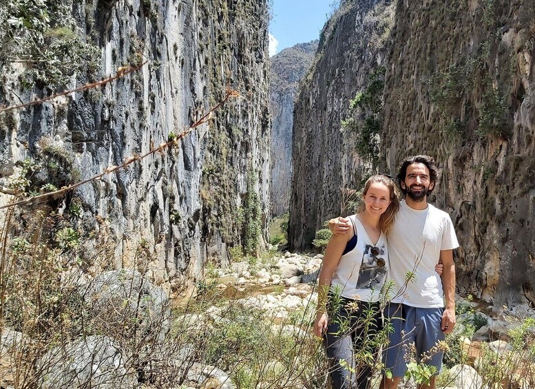 A couple hiking in a rocky canyon with steep cliffs and sparse vegetation. 1