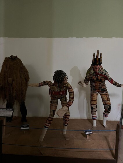 Three mannequins in traditional attire, one with a headdress and another with a mask. 3