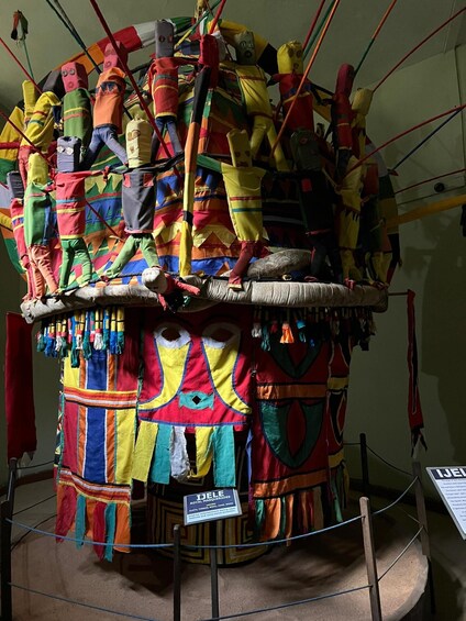 A colorful display of traditional masks and costumes, including a prominent yellow and red outfit with intricate patterns. 1