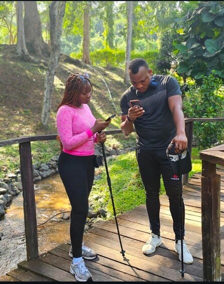Two people standing on a wooden deck by a stream in a forested area. 1