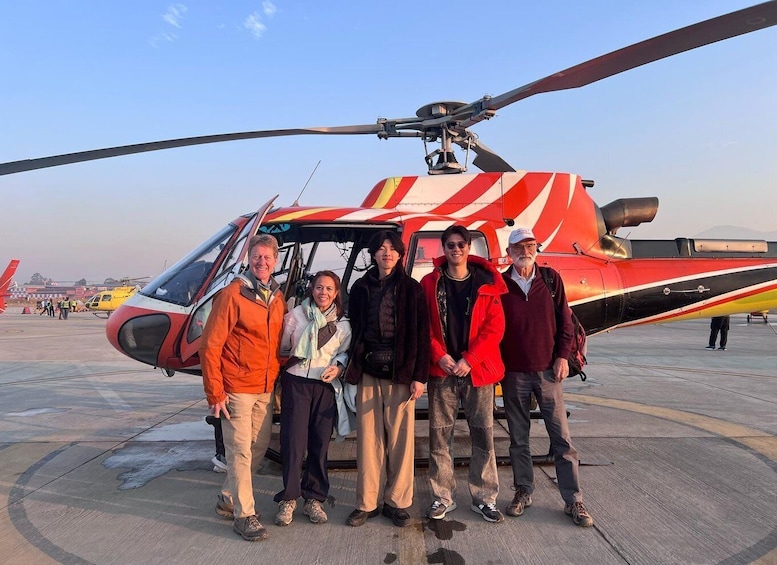 A group of people standing in front of a red and white helicopter on a tarmac. 1