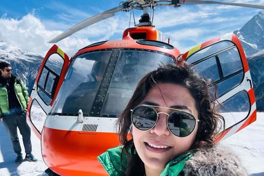 A person in a green jacket standing in front of a red and white helicopter on a snowy mountain. 4