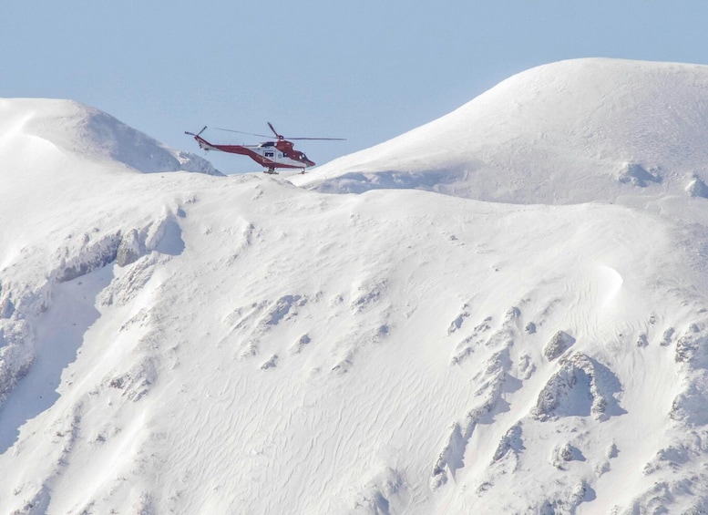 A red helicopter flying over a snow-covered mountain. 5