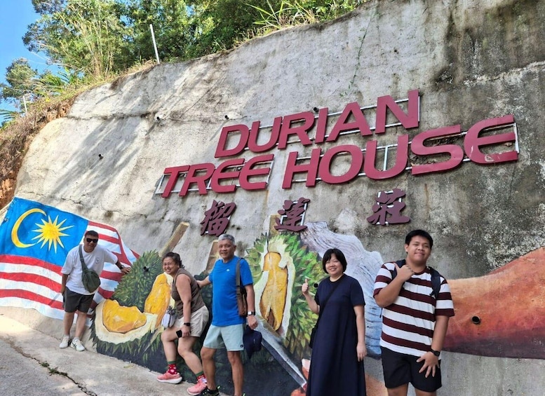 A group of people standing in front of a wall with the Durian Tree House sign and a mural of a durian tree. 1